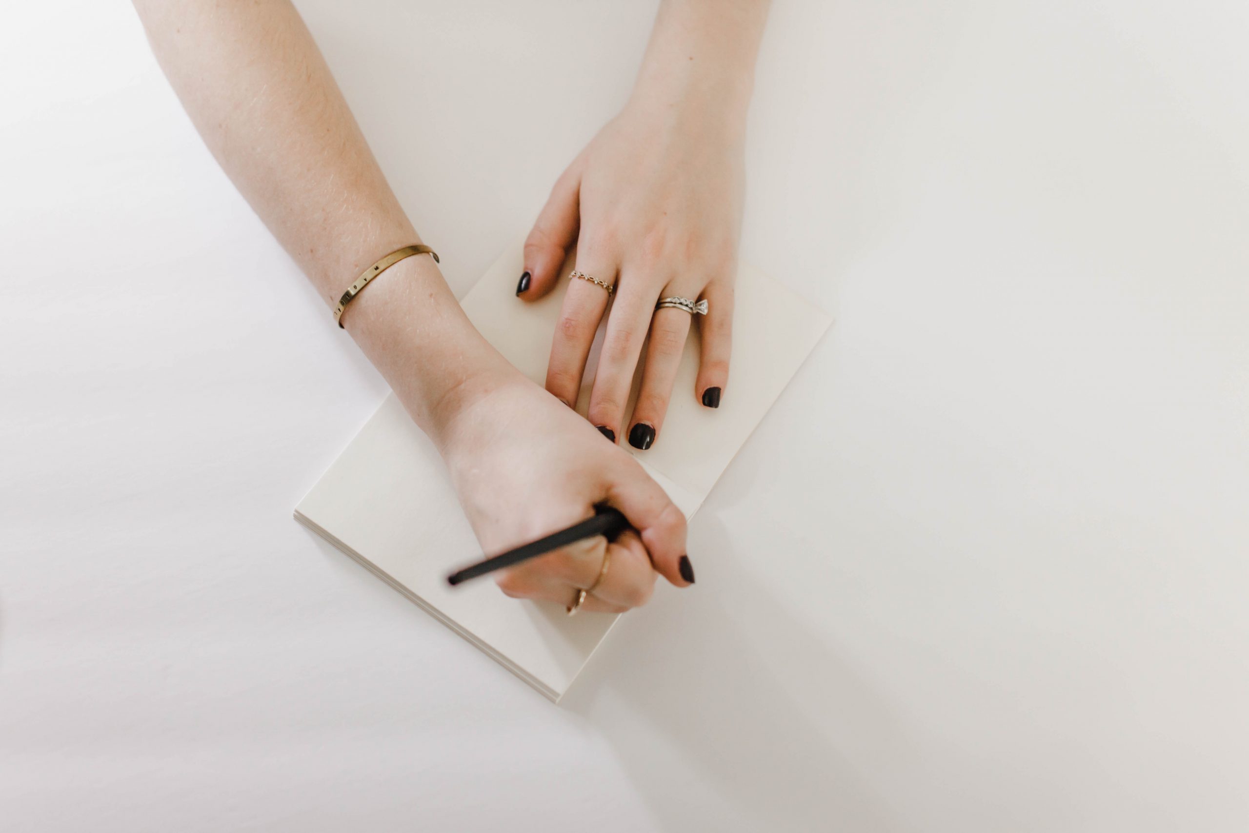 Hands writing notes with a pen in a small notebook on a white desk