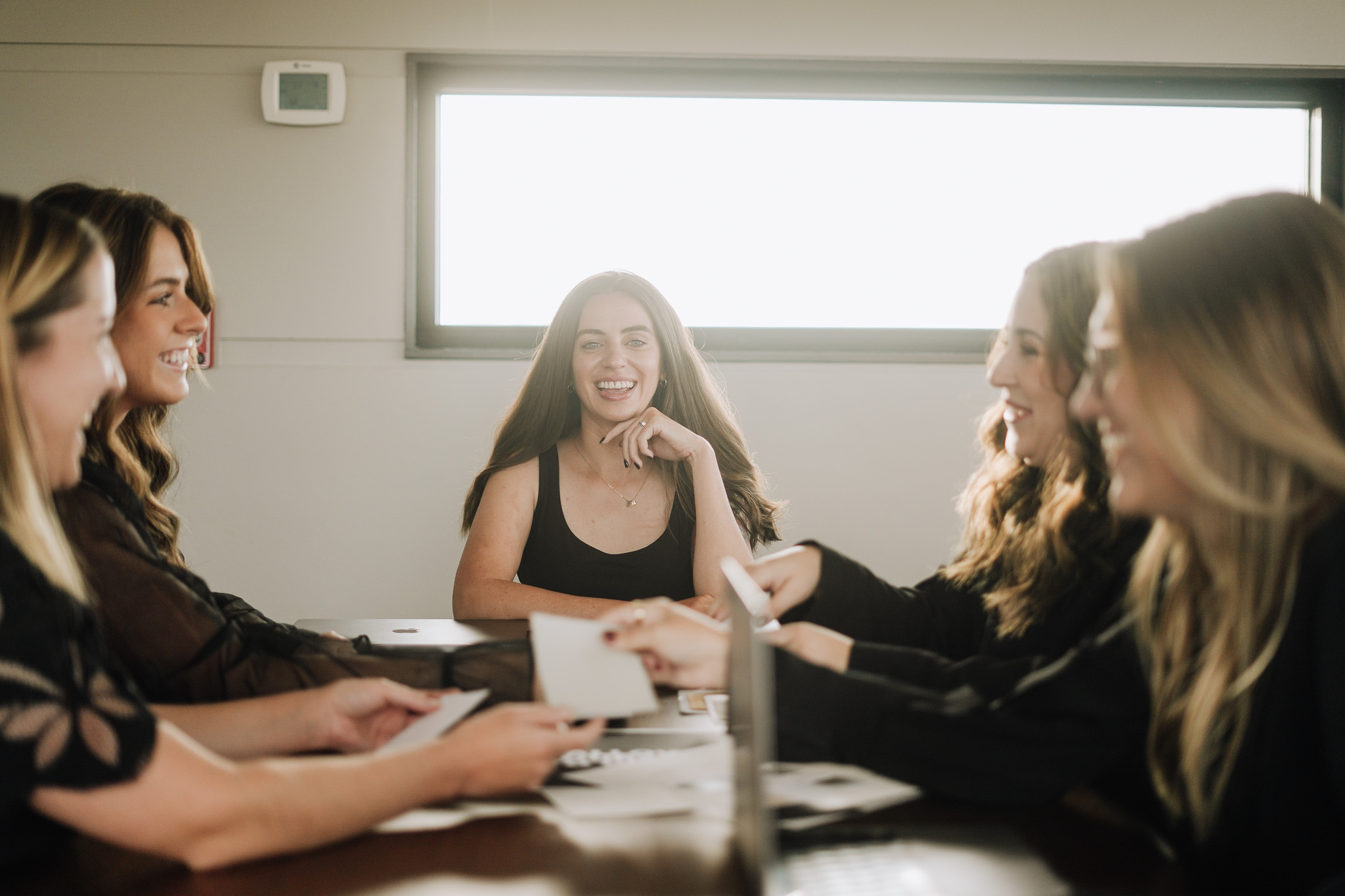 Five women talk and smile around a table during a team meeting, the kind of group a strong therapist bio introduces